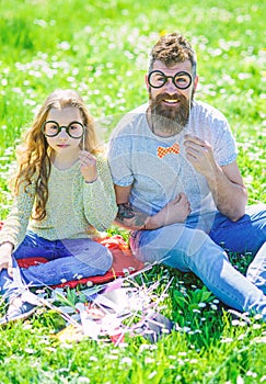 Dad and daughter sits on grass at grassplot, green background. Child and father posing with eyeglases photo booth