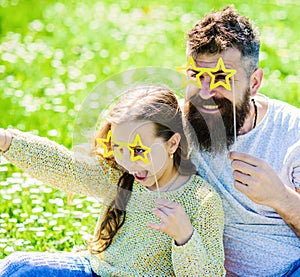 Dad and daughter sits on grass at grassplot, green background. Child and father posing with star shaped eyeglases photo photo