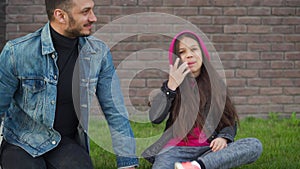 Dad and daughter are sitting, having fun and chewing bubble gum against the backdrop of grass and a brick wall. Concept