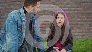 Dad and daughter are sitting, having fun and chewing bubble gum against the backdrop of grass and a brick wall. Concept