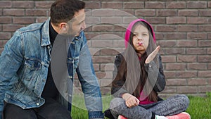 Dad and daughter are sitting, having fun and chewing bubble gum against the backdrop of grass and a brick wall. Concept