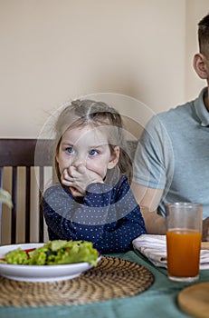 Dad and daughter are sitting in the kitchen at the table and eating vegetables. Vegetarian family