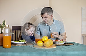 Dad and daughter are sitting in the kitchen at the table and eating vegetables. Vegetarian family