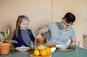 Dad and daughter are sitting in the kitchen at the table and eating vegetables. Vegetarian family