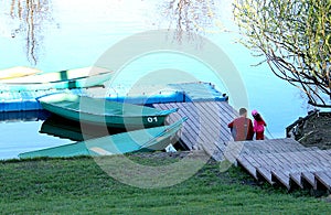 Dad and daughter are sitting on the river bank near the boat station