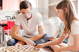 Dad, daughter and son play checkers at home together