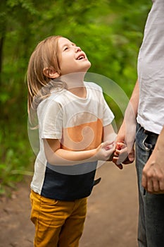 Dad and daughter walk in the forest in summer, the girl holds dad's hand