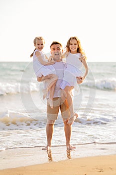 Dad with daughters walking along sea-shore in windy weather. fun family