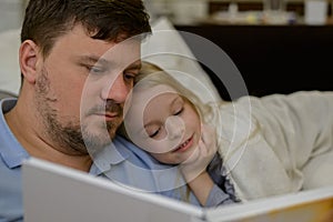 dad entertains the child during illness: he looks, reads a book, a photo book with his daughter home. The father