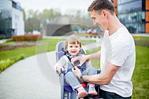 Dad fastens his daughter`s seat belts before riding a bike.