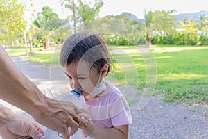 Dad giving bottle water to cute little asian girl, wearing safety face mask under chin