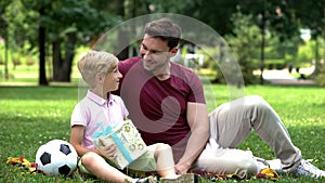 Dad giving present to son for goal in football match, encouraging boy for sport