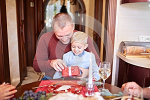 Dad giving a red gift to little son on a festive background. Family Christmas presents concept.