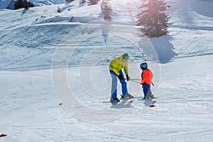 Dad glide backwards teaching little child to ski using poles