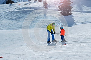 Dad glide backwards teaching little child to ski using poles photo