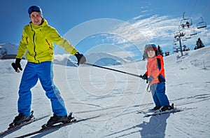 Dad go downhill teach child to ski connected by poles