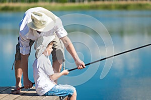 Dad helps his son catch fish with a fishing rod on the river