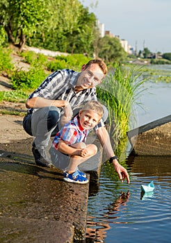 Dad helps the Little Boy to lower the paper boat to the water in