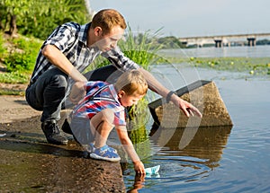 Dad helps the Little Boy to lower the paper boat to the water in