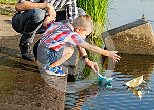 Dad helps the Little Boy to lower the paper boat to the water. D