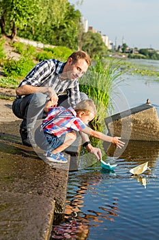 Dad helps the Little Boy to lower the paper boat to the water. D