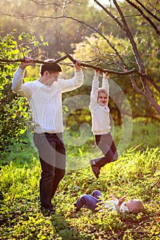 Dad helps support the boy hanging on the branch of a tree, suns