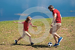 Dad with his little cute son are having fun and playing football on green grassy summer lawn. Football soccer sport