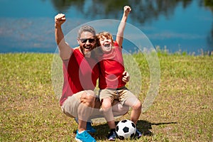 Dad with his little cute son are having fun and playing football on green grassy summer lawn. Football soccer sport