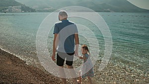 Dad and his little daughter are walking along the beach of the sea.