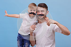 Dad and his son are standing side by side on a blue background. Front view