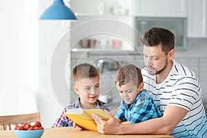 Dad and his sons reading interesting book in kitchen. Space for