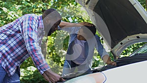 Dad hitting upside head scolding son repairing car together, child upbringing