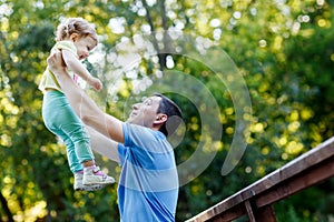 Dad holds baby daughter in his arms high in park