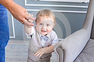 Dad holds baby son 1 year old by the hand in a photo Studio on a gray background, family day, father`s day