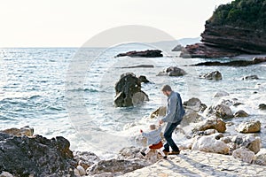 Dad holds the hand of a little girl, going down with her along a stone path to a pebble beach to the water against a