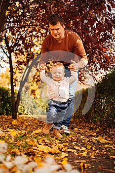 dad holds hands and teaches to walk of son on the lawn. first steps