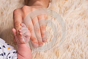 Dad holds in his hands a small baby hand. Small hand of a newborn baby in large hands of dad. Baby holds father& x27;s finger