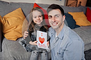 Dad hugs daughter holding greeting card. Father\'s Day concept. Family happiness and love