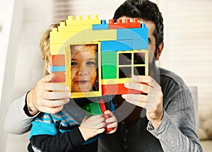 Dad and kid hide behind house wall made of blocks