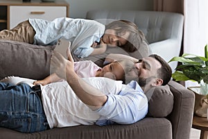 Dad with kids lying on couch spend time use smartphone