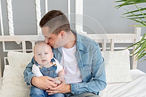 Dad kisses baby at home on the bed, happy fatherhood or father`s day