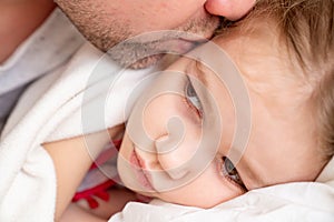 Dad kisses little sick daughter sleeping on bed.