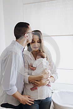 Dad kissing mother. Mom holding newborn baby. Happy family. Mother, father and son