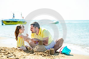 Dad and little girl play, sculpt sand castles on the beach and fool around on the sea coast. Family vacation at sea with