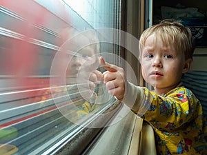 Dad, look - the train! A little blond-haired boy of three years rides on a train, eats candy and looks out the window