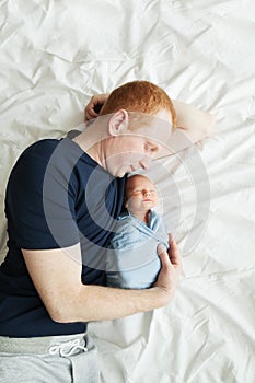 Dad is lying in bed with his newborn son.