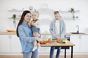 Dad making salad while kid eating banana on mommy's hands