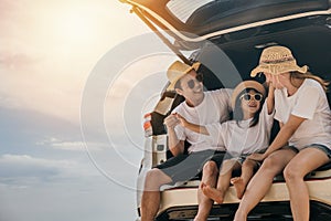 Dad, mom and daughter enjoying road trip sitting on back car