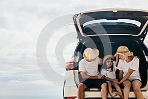 Dad, mom and daughter enjoying road trip sitting on back car