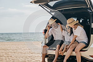 Dad, mom and daughter enjoying road trip sitting on back car